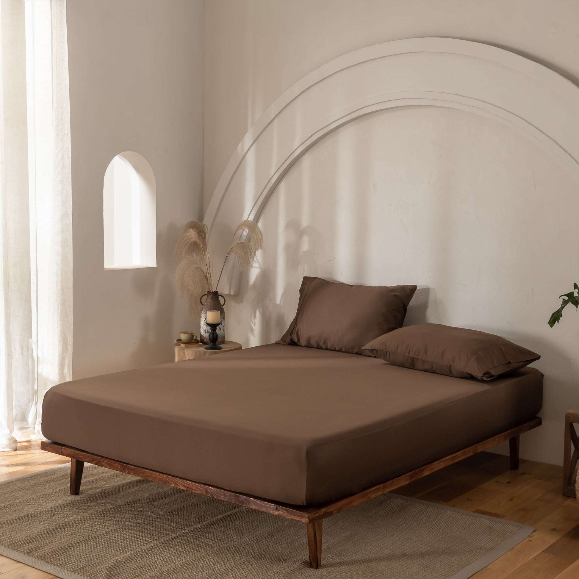 Brown bed with matching pillows in a minimalistic room with wooden floor and white walls.